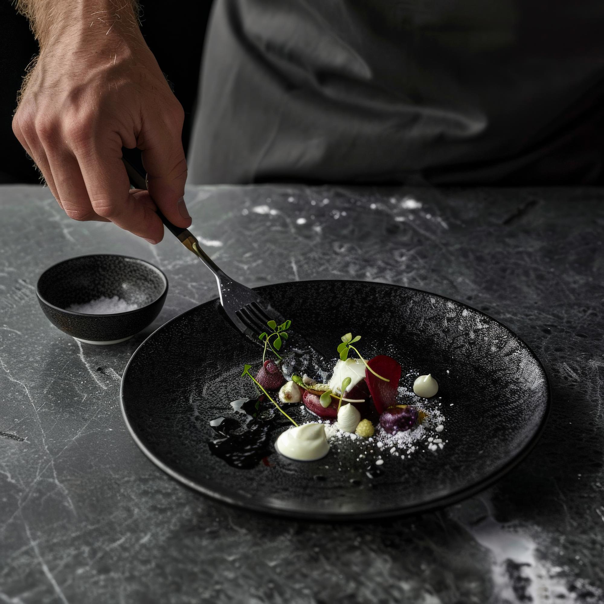 Chef plating a refined dish in a dark studio